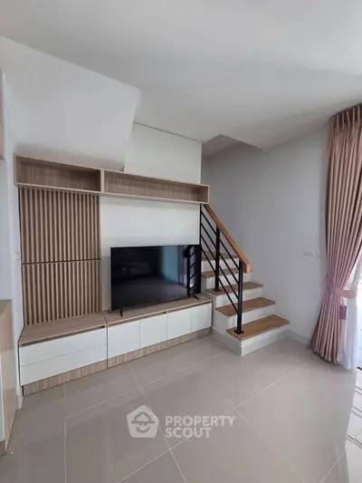 Modern living room with sleek TV unit and staircase, featuring elegant curtains and natural light.