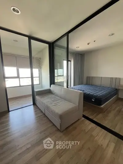 Modern bedroom with glass partition and cozy sofa, featuring wooden flooring and large windows for natural light.