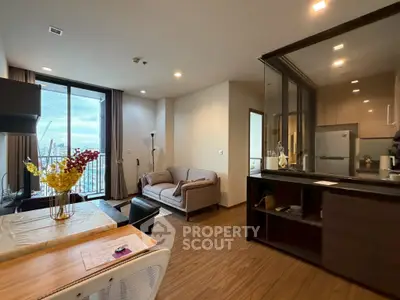 Modern living room with open kitchen and city view, featuring stylish furniture and large windows.
