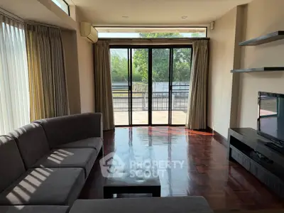 Spacious living room with large windows and balcony access, featuring modern furniture and natural light.