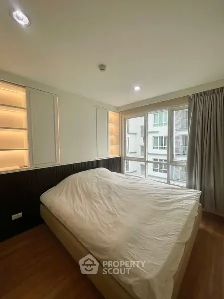 Modern bedroom with large windows and built-in shelving, offering ample natural light.