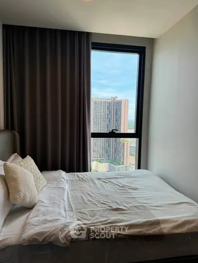 Cozy bedroom with city view from window, featuring elegant bedding and modern design.