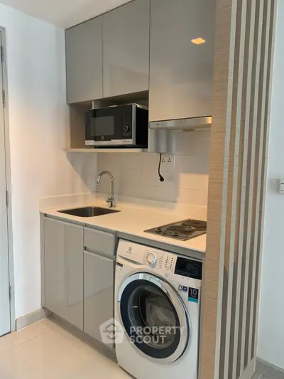 Modern compact kitchen with sleek cabinetry, built-in microwave, and washing machine in a stylish apartment.