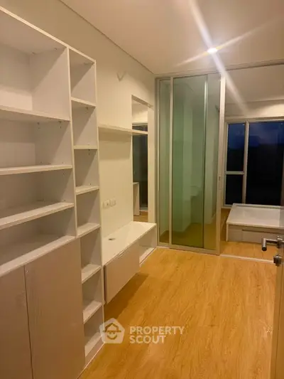 Modern apartment interior with built-in shelves and wooden flooring, featuring a glass partition.