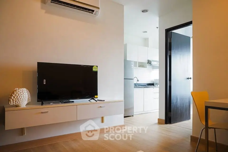 Modern living room with sleek TV setup and view into a stylish kitchen.