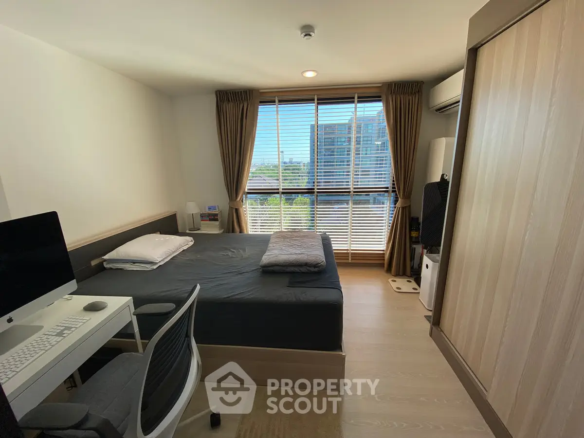 Modern bedroom with large window and natural light, featuring a workspace and stylish decor.