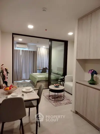 Modern open-plan living room with dining area and bedroom, featuring elegant decor and natural light.