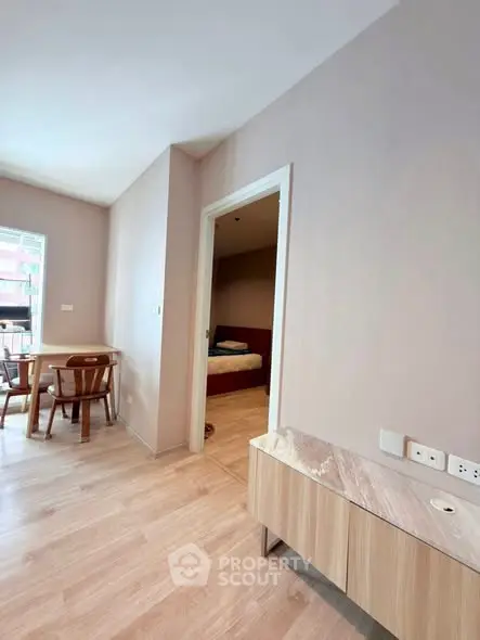 Modern apartment interior with wooden flooring, dining area, and bedroom entrance.