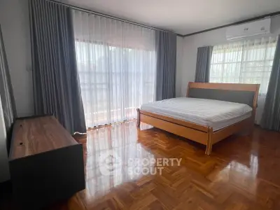 Spacious bedroom with wooden flooring and large windows for natural light