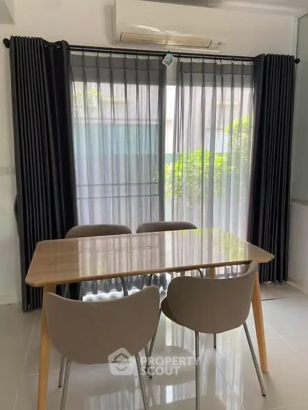 Modern dining area with sleek table and chairs, large windows with curtains, and air conditioning unit.