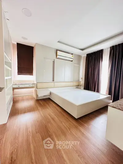 Spacious modern bedroom with wooden flooring and large windows for natural light.