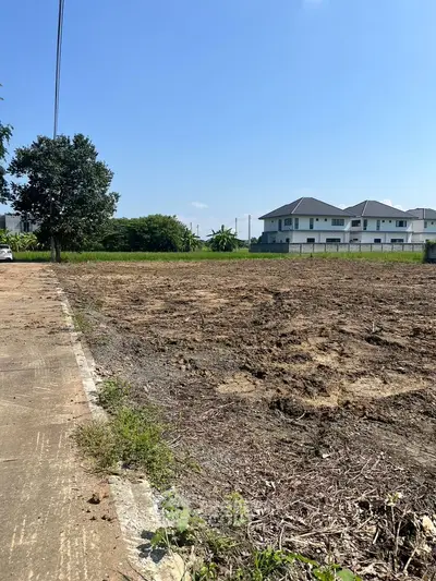 Spacious vacant land plot with potential for residential development, surrounded by greenery and nearby houses.