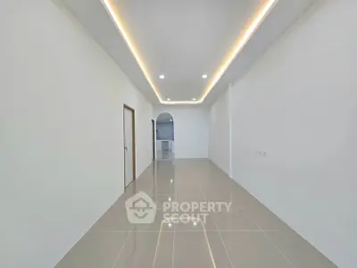 Spacious modern interior with sleek tile flooring and recessed lighting, leading to a kitchen area.