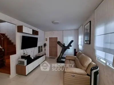 Modern living room with treadmill, leather sofa, and wall-mounted TV in a stylish home.