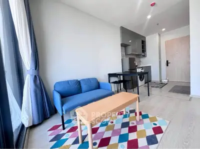 Modern living room with blue sofa, colorful rug, and open kitchen layout in bright apartment.