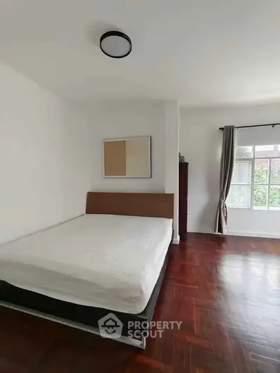Spacious bedroom with hardwood floors and large window offering natural light.