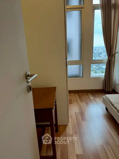 Cozy bedroom with wooden flooring and city view from large windows.