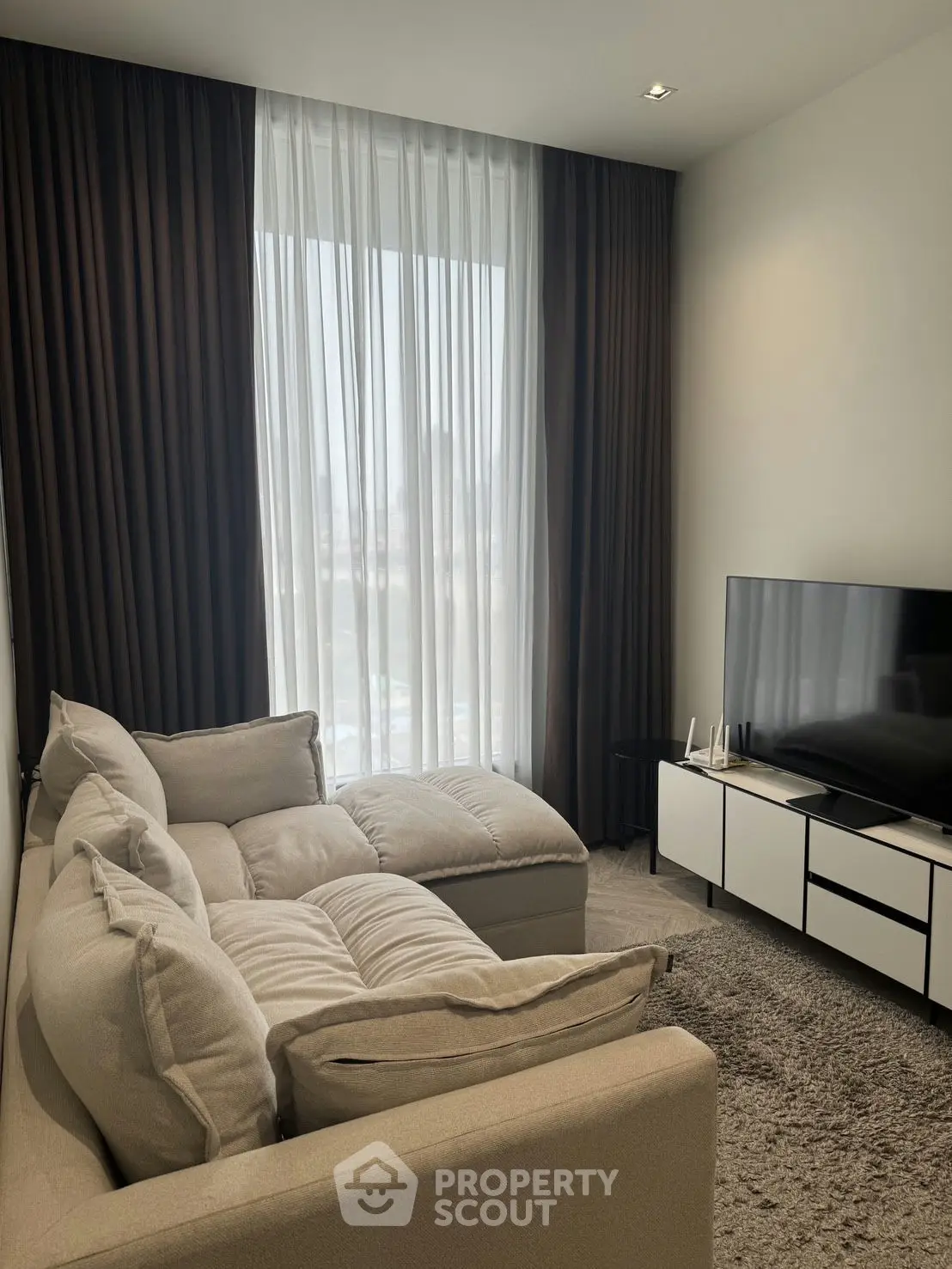 Modern living room with cozy sectional sofa and large TV, featuring floor-to-ceiling windows and elegant curtains.