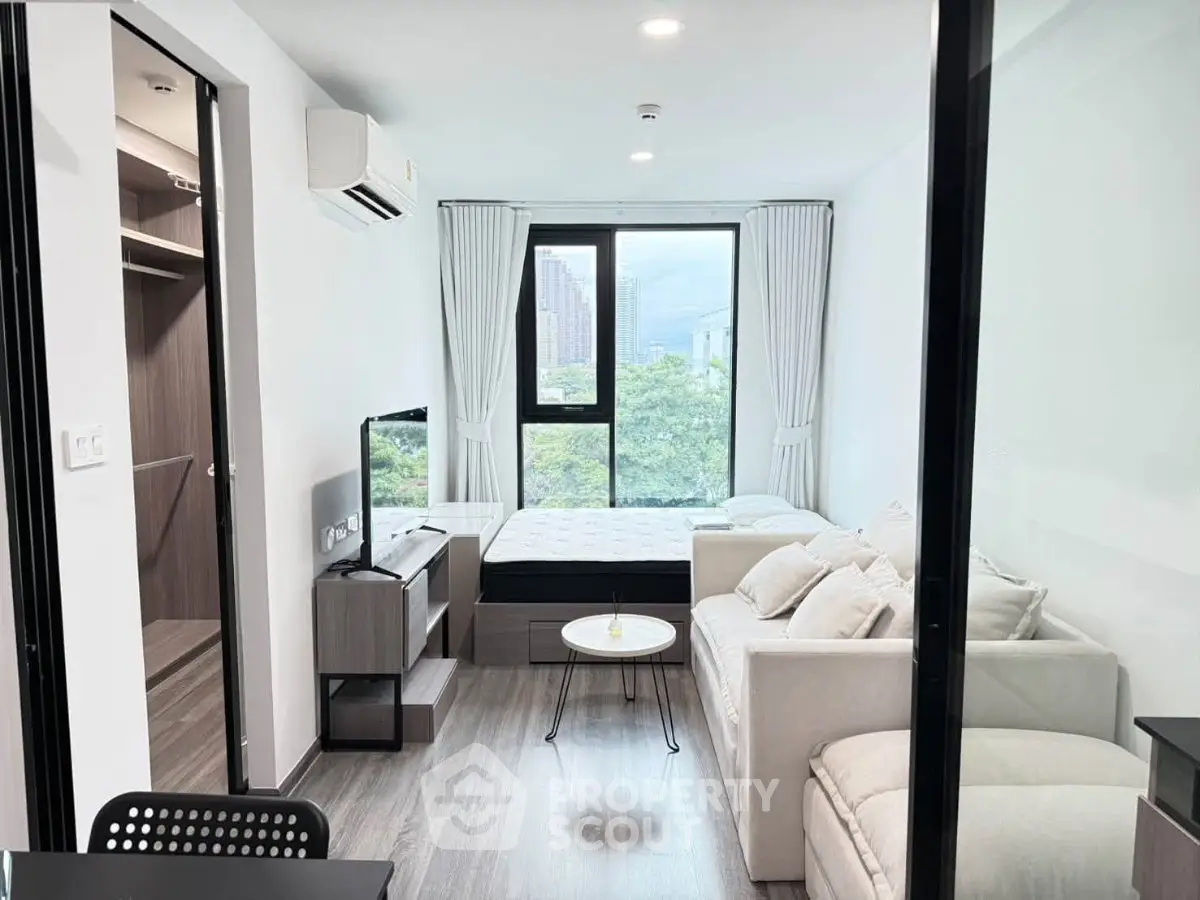 Modern studio apartment with large windows and stylish furnishings, offering a bright and cozy living space.