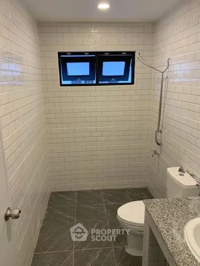 Modern bathroom with sleek tile design and compact layout, featuring a window for natural light.