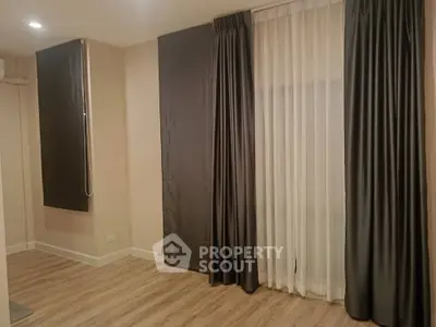 Spacious and elegantly designed living room with modern wooden flooring and large windows draped with luxurious curtains, perfect for comfortable urban living.