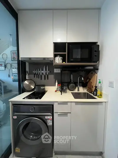 Compact modern kitchen with washing machine and microwave, ideal for urban living.
