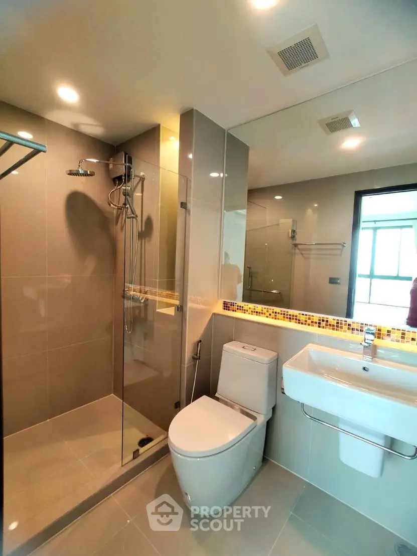 Modern bathroom with glass shower, sleek fixtures, and large mirror in a contemporary home.