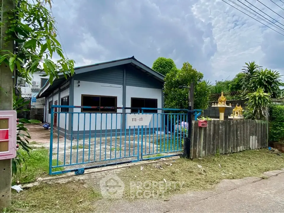 Charming single-story house with blue gate and lush greenery, perfect for serene living.