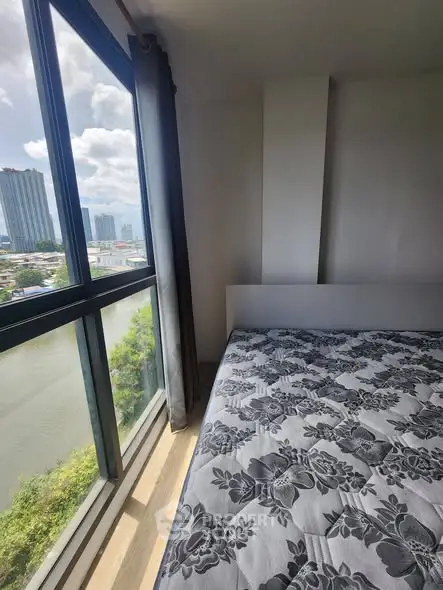 Bright bedroom with large window offering stunning city and river views, featuring a comfortable bed and modern decor.
