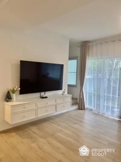 Spacious living room with modern TV setup and large window view