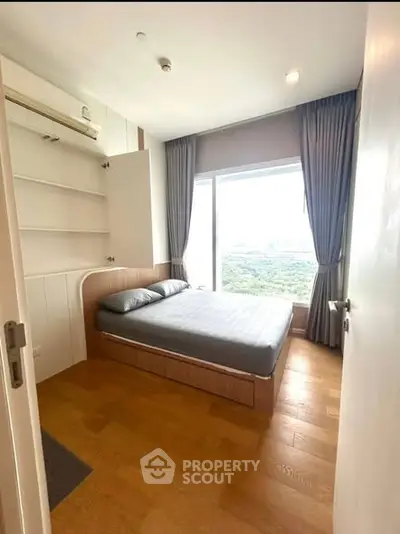 Cozy bedroom with large window offering stunning city view and ample natural light.