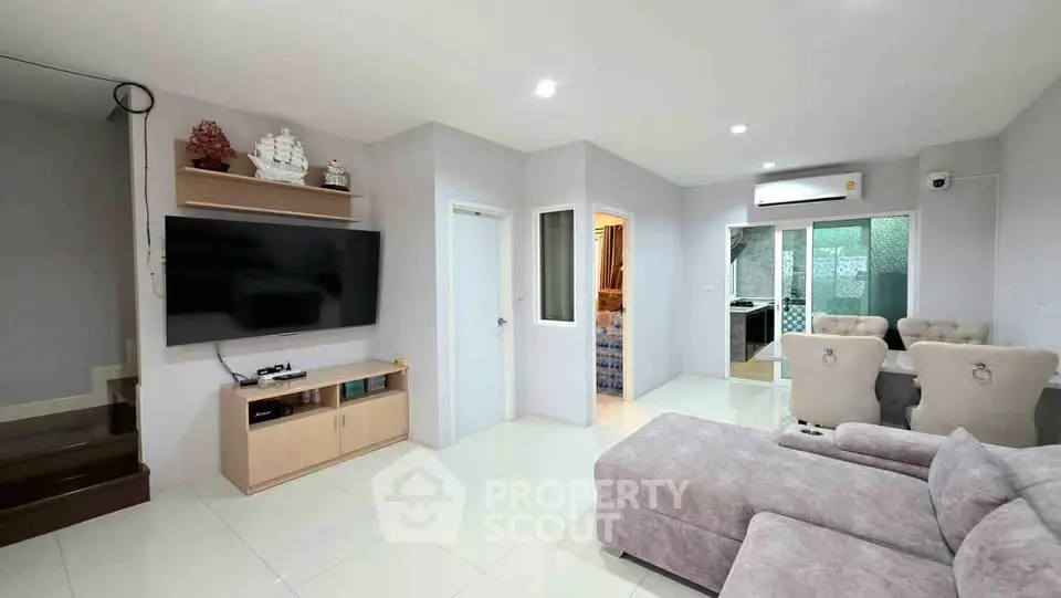 Spacious modern living room with plush sectional sofa and wall-mounted TV, leading to dining area and kitchen.