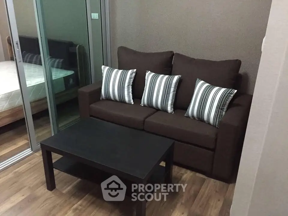 Cozy living room with brown sofa and striped cushions, adjacent to a bedroom with glass sliding doors.