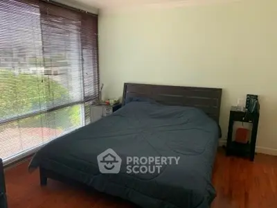 Spacious bedroom with large windows and wooden flooring, offering a serene and cozy atmosphere.