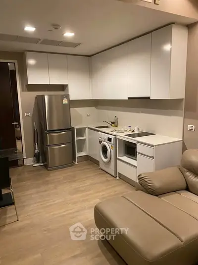 Modern kitchen with sleek cabinets, stainless steel fridge, and integrated washing machine in cozy apartment.