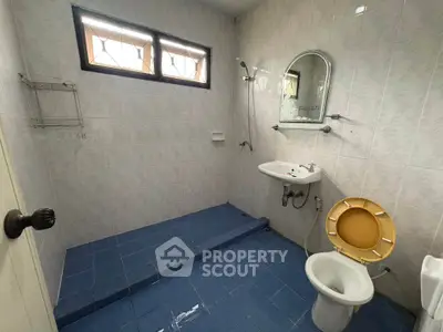 Spacious bathroom with blue tiled floor and elevated shower area, featuring a wall-mounted sink and toilet.