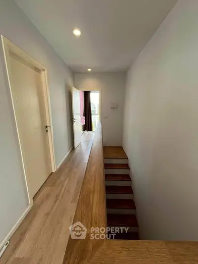 Modern hallway with wooden flooring and staircase leading to a bright room with balcony.