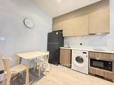 Modern kitchen with washing machine, fridge, and dining set in sleek apartment.