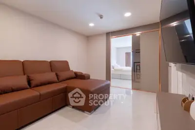 Modern living room with brown sectional sofa and wall-mounted TV, leading to a bright bedroom.