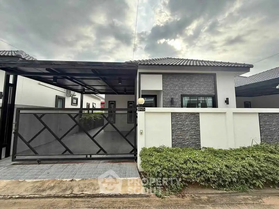 Modern single-story house with sleek design and gated entrance under a cloudy sky.