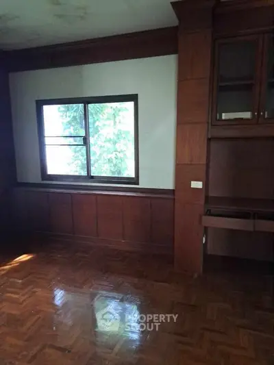 Spacious room with wooden flooring and large window, ideal for customization.