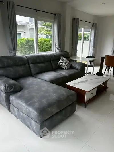 Spacious living room with modern gray sectional sofa and elegant marble coffee table, featuring large windows and natural light.