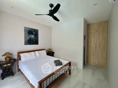 Spacious bedroom with polished tile flooring, modern ceiling fan, and wooden wardrobe, complemented by minimalist decor and artwork.