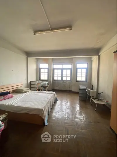 Spacious bedroom with large windows and wooden flooring, offering ample natural light and potential for customization.