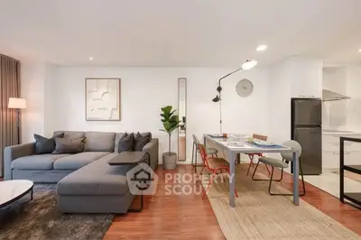 Modern living room with stylish furniture and open dining area, featuring a cozy gray sofa and sleek dining table.