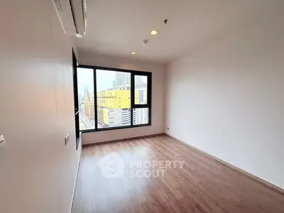 Spacious empty room with large window offering city view and wooden flooring.
