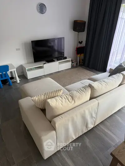 Modern living room with stylish decor, featuring a cozy white sofa, sleek TV setup, and elegant flooring.