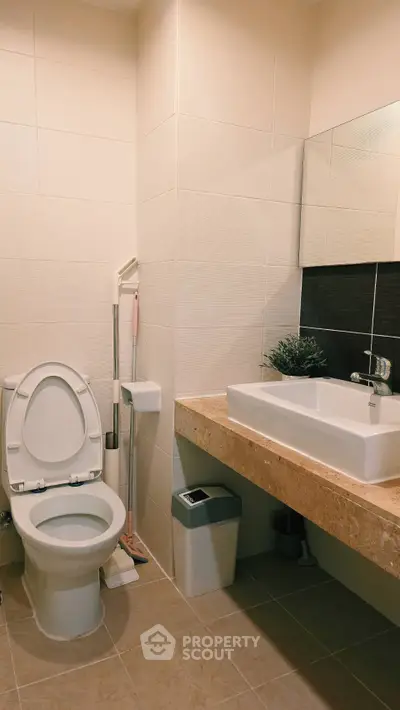 Modern bathroom with sleek sink and toilet, featuring neutral tiles and a minimalist design.