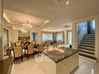 Luxurious open-plan living and dining area with elegant chandelier and modern staircase.