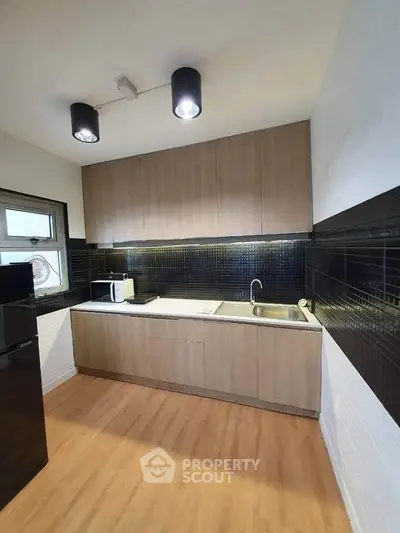 Modern kitchen with sleek cabinets and black tile backsplash, featuring a microwave and sink.
